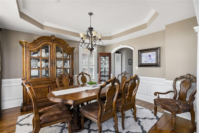 dining space featuring dark wood-style floors, arched walkways, a raised ceiling, and wainscoting