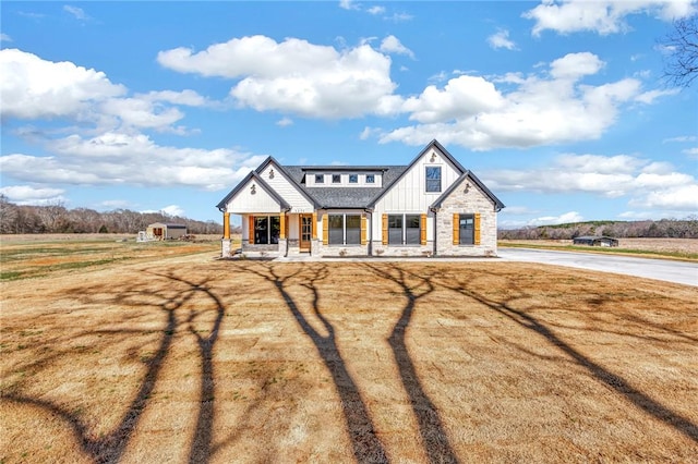 modern farmhouse with stone siding, a porch, board and batten siding, and a front lawn