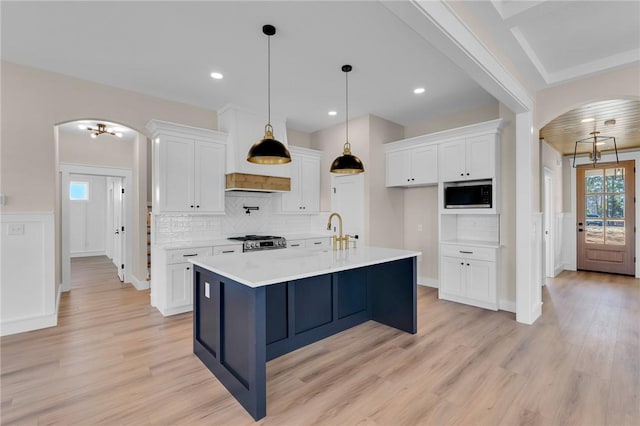 kitchen with arched walkways, range, light wood-style flooring, stainless steel microwave, and white cabinetry