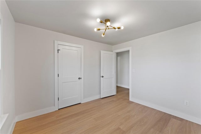 unfurnished bedroom featuring light wood-style flooring, baseboards, and an inviting chandelier