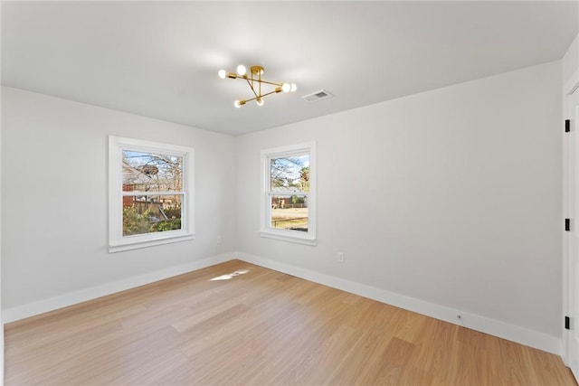 unfurnished room featuring baseboards, light wood-style flooring, visible vents, and a notable chandelier