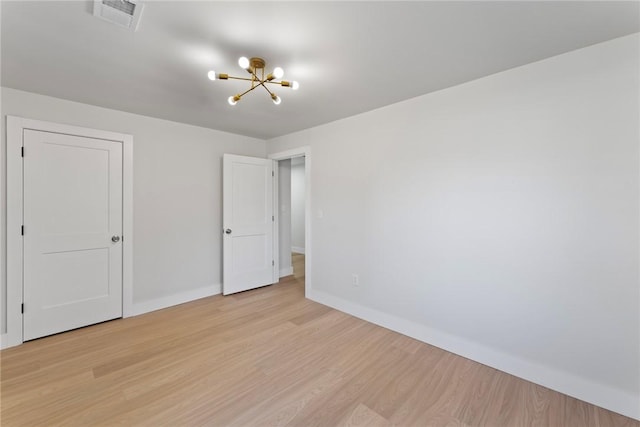 empty room featuring light wood finished floors, baseboards, visible vents, and a notable chandelier