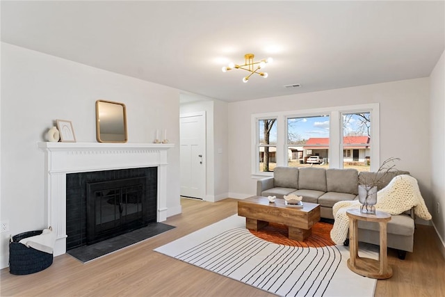 living room featuring a brick fireplace, baseboards, a chandelier, and light wood-style floors