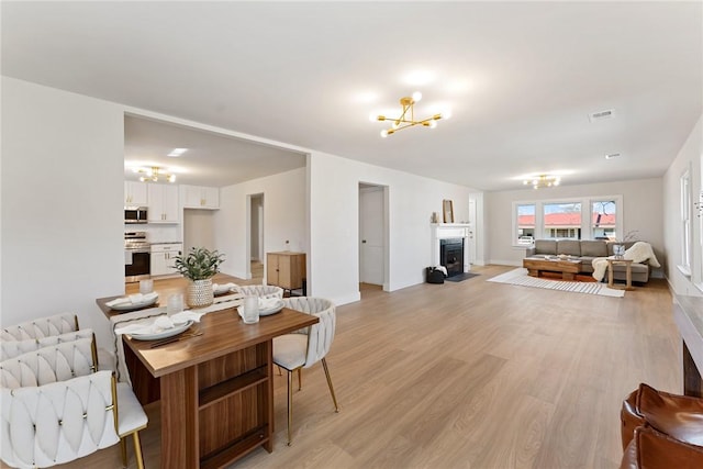 dining area with a notable chandelier, visible vents, a fireplace with flush hearth, light wood-type flooring, and baseboards