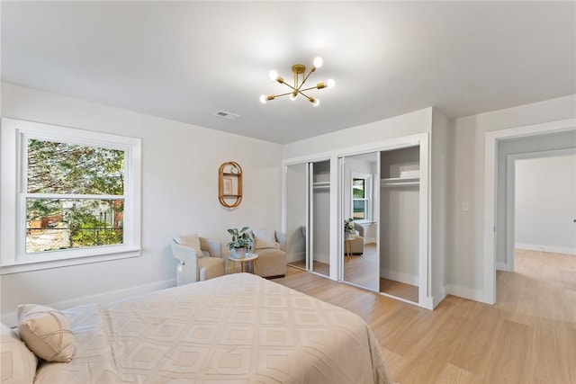 bedroom with light wood-type flooring, an inviting chandelier, visible vents, and baseboards