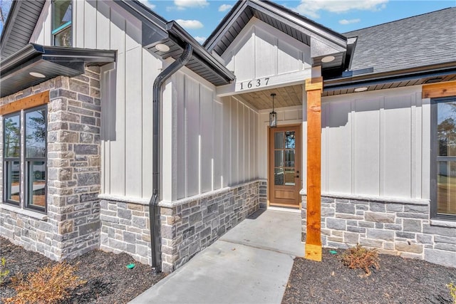 entrance to property featuring stone siding, a shingled roof, and board and batten siding