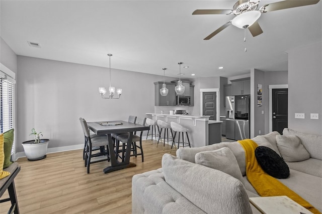 living area featuring visible vents, baseboards, light wood finished floors, recessed lighting, and ceiling fan with notable chandelier