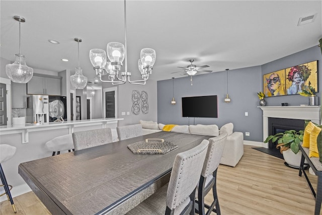 dining area with a ceiling fan, visible vents, light wood finished floors, baseboards, and a fireplace with flush hearth