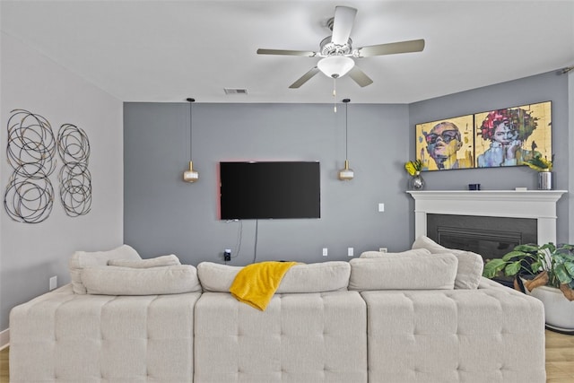 living area featuring ceiling fan, visible vents, wood finished floors, and a glass covered fireplace