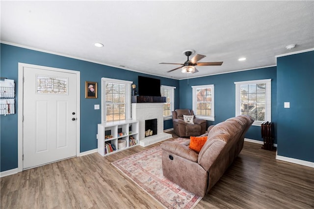 living room featuring a brick fireplace, baseboards, ornamental molding, and wood finished floors