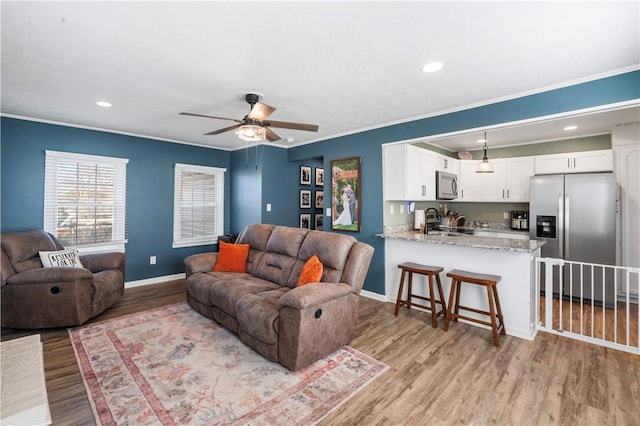 living area featuring baseboards, recessed lighting, light wood-style flooring, and crown molding