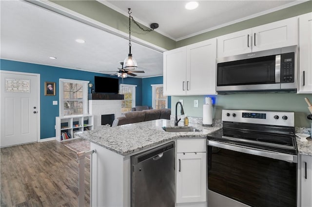 kitchen with appliances with stainless steel finishes, ornamental molding, a peninsula, a fireplace, and a sink