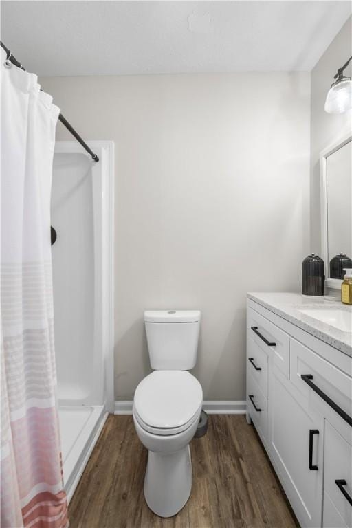 bathroom featuring toilet, a stall shower, wood finished floors, and vanity