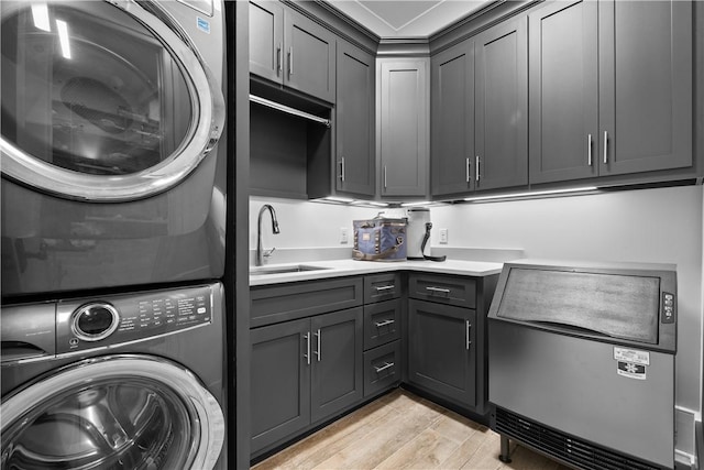 laundry room featuring light wood finished floors, cabinet space, a sink, and stacked washer and clothes dryer