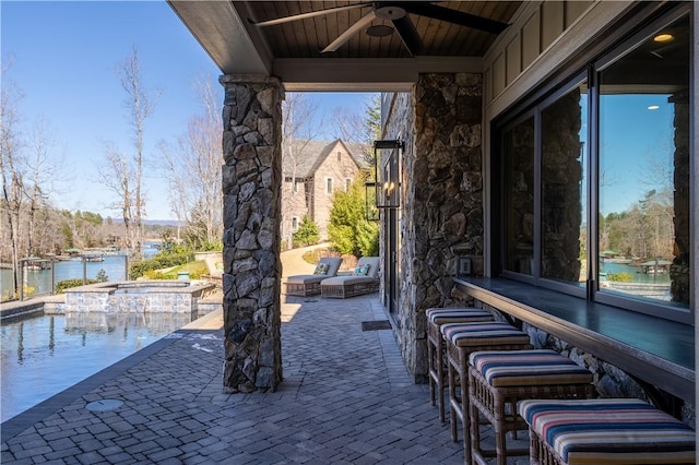 view of patio / terrace with a pool with connected hot tub, a water view, and a ceiling fan