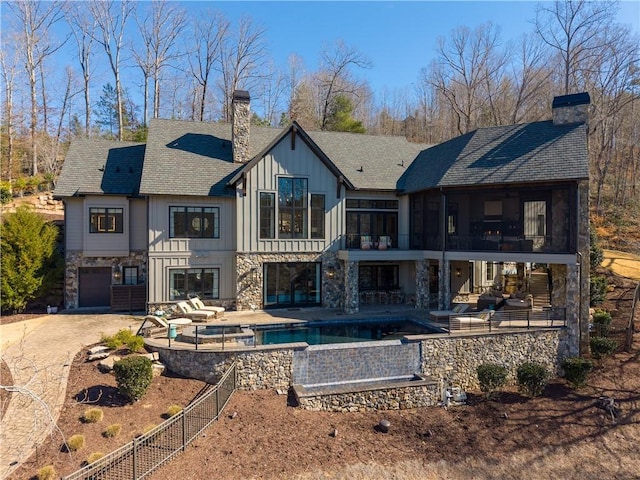 back of property featuring board and batten siding, a sunroom, a patio, and a chimney