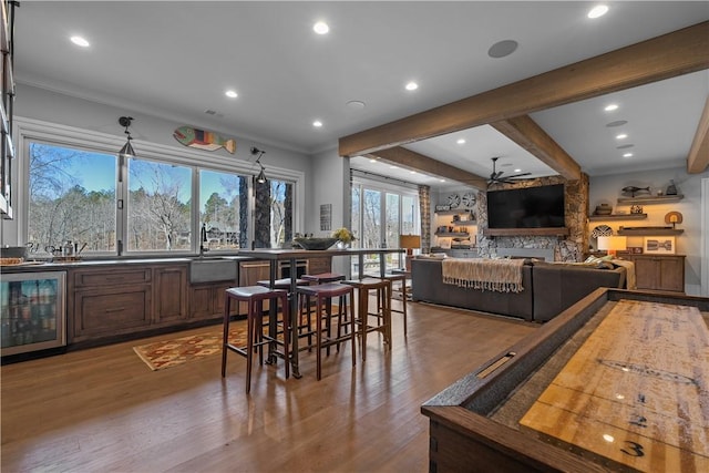 dining space featuring wine cooler, indoor wet bar, ornamental molding, wood finished floors, and beamed ceiling