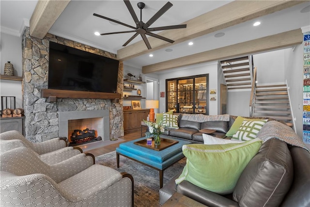 living room featuring ceiling fan, a fireplace, wood finished floors, stairway, and beamed ceiling