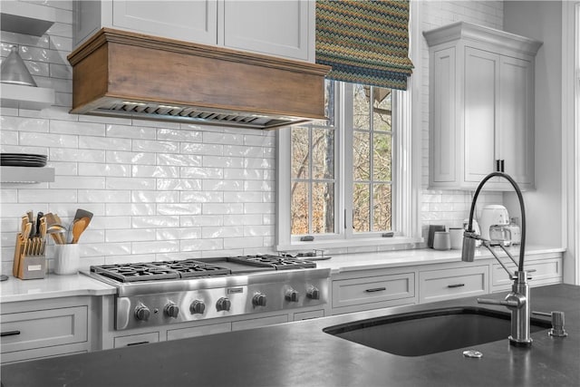 kitchen featuring stainless steel gas cooktop, custom range hood, backsplash, white cabinets, and a sink