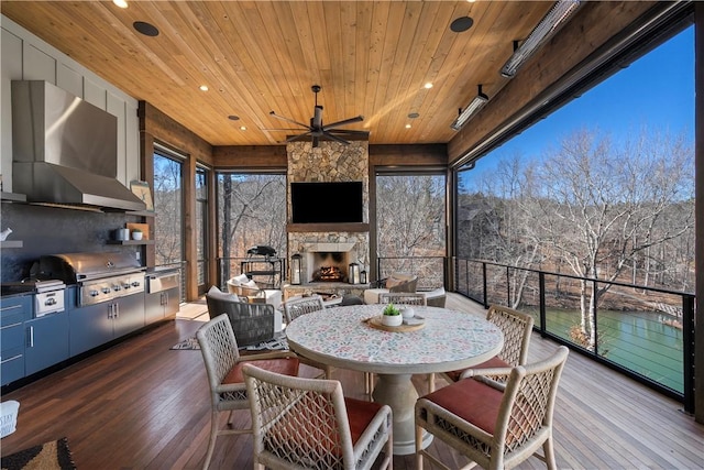 wooden deck featuring outdoor dining area, an outdoor stone fireplace, area for grilling, a grill, and a ceiling fan