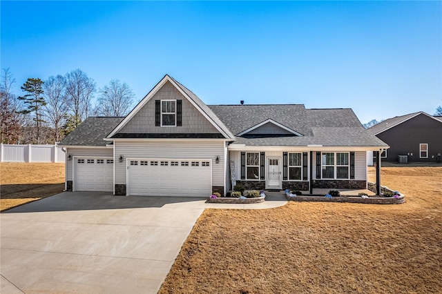 craftsman-style house featuring a shingled roof, concrete driveway, fence, stone siding, and a front lawn