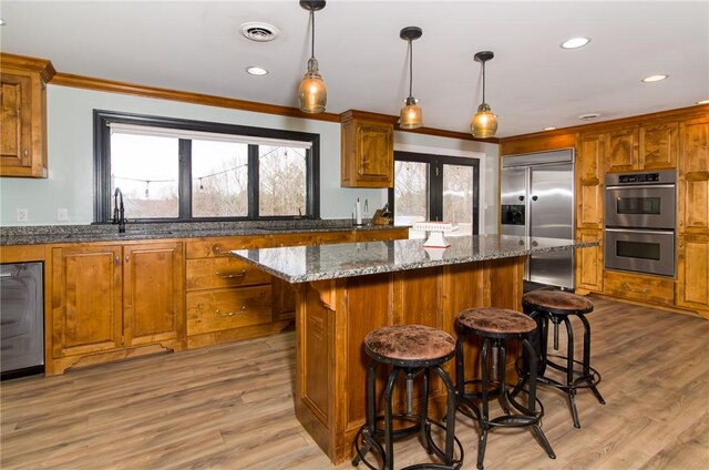 kitchen featuring stainless steel appliances, a sink, visible vents, a center island, and brown cabinetry