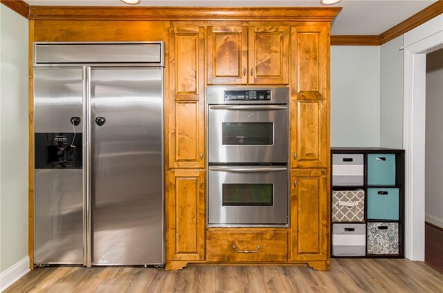 kitchen with stainless steel appliances, brown cabinetry, ornamental molding, and light wood-style flooring