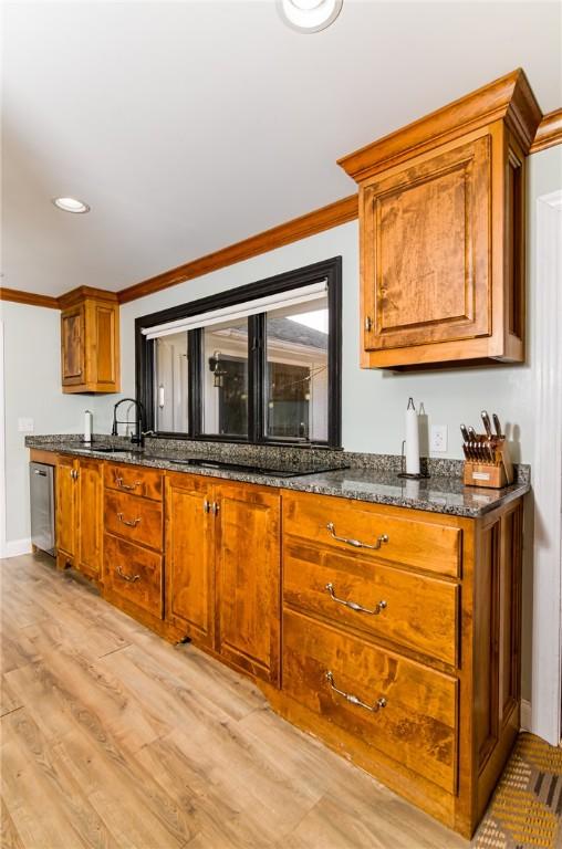 kitchen featuring dishwasher, brown cabinets, crown molding, light wood-type flooring, and a sink