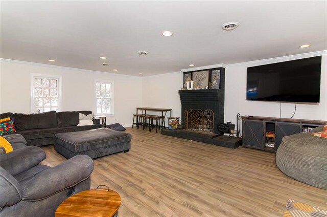 living room featuring a brick fireplace, visible vents, wood finished floors, and ornamental molding