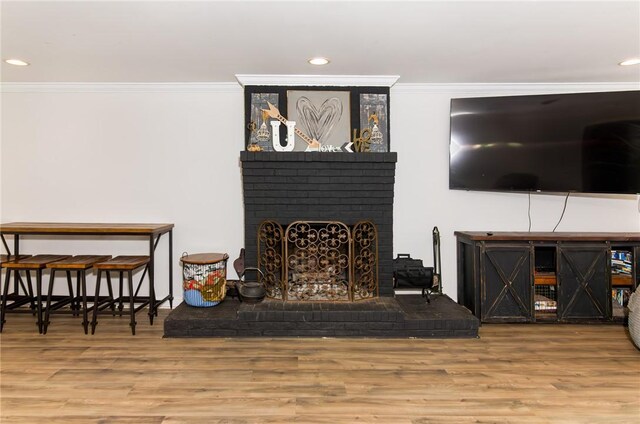 living area with ornamental molding, a brick fireplace, and wood finished floors