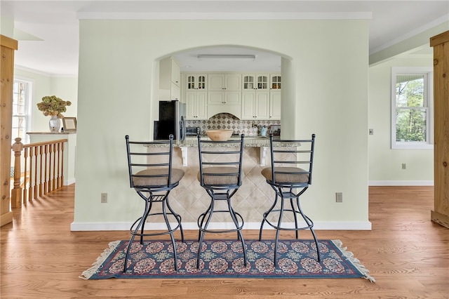 dining space with ornamental molding, arched walkways, light wood-style flooring, and baseboards