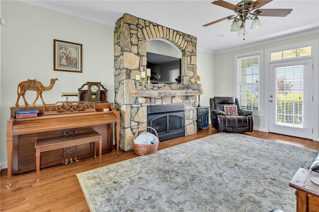 living area with a fireplace, crown molding, a ceiling fan, wood finished floors, and baseboards