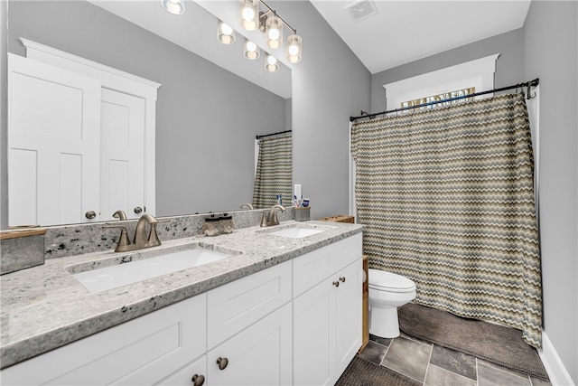 full bathroom with toilet, double vanity, visible vents, and a sink