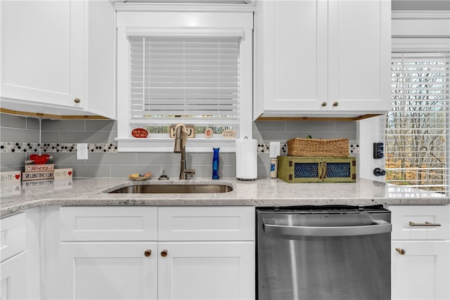 kitchen featuring dishwasher, tasteful backsplash, a sink, and white cabinetry