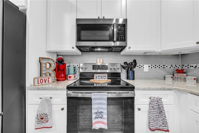 kitchen with tasteful backsplash, appliances with stainless steel finishes, white cabinets, and light stone counters