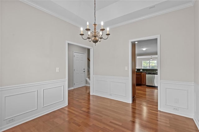 unfurnished dining area featuring stairs, ornamental molding, a wainscoted wall, and wood finished floors