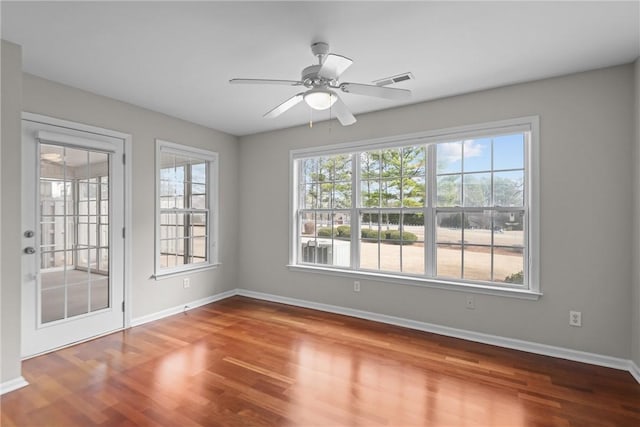 spare room with a ceiling fan, wood finished floors, visible vents, and baseboards