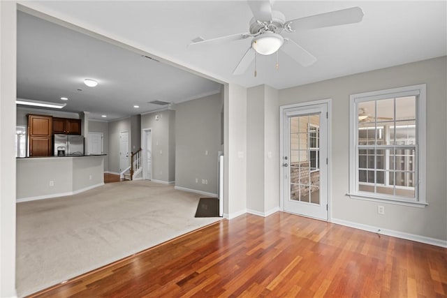 unfurnished living room with baseboards, a ceiling fan, wood finished floors, stairs, and crown molding