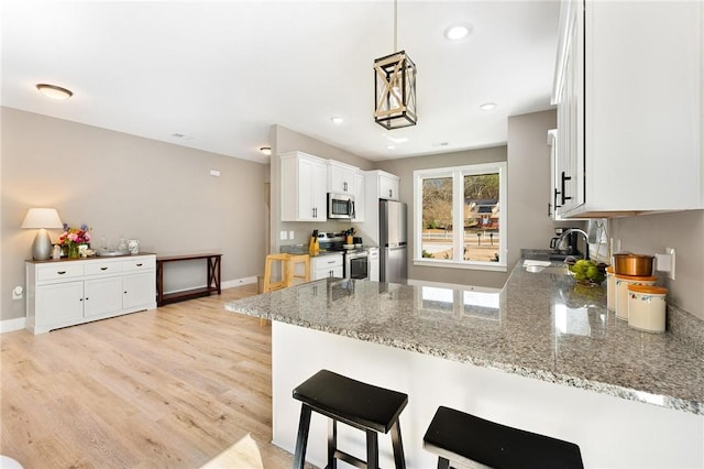 kitchen with stainless steel appliances, white cabinetry, a peninsula, and light stone counters