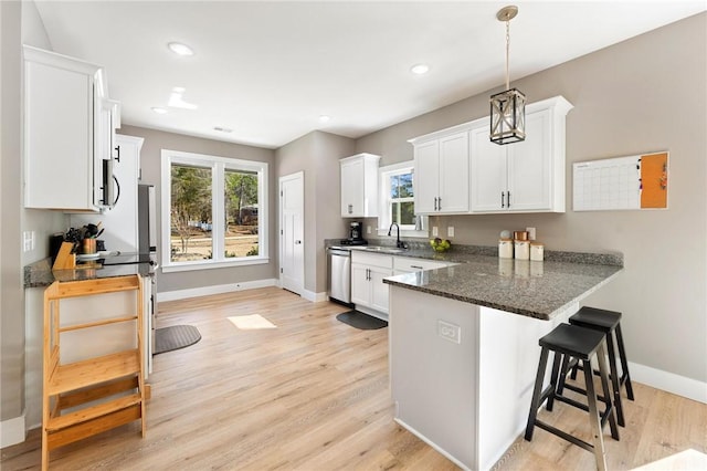 kitchen with a breakfast bar area, light wood-style flooring, a peninsula, white cabinets, and stainless steel dishwasher