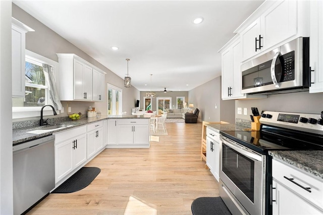 kitchen featuring white cabinets, open floor plan, a peninsula, stainless steel appliances, and a sink