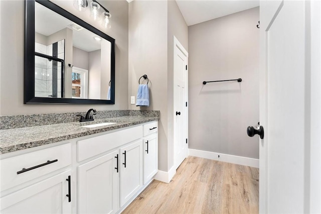 bathroom with tiled shower, vanity, baseboards, and wood finished floors