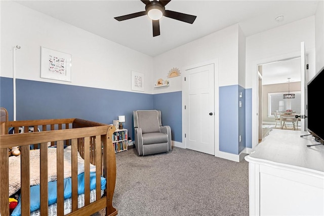 carpeted bedroom with a nursery area, baseboards, and a ceiling fan