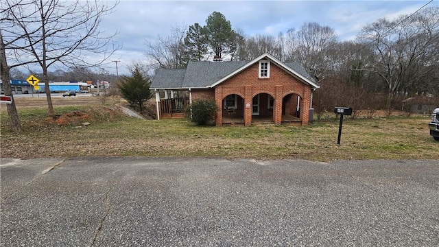 view of front of house with a porch, brick siding, a front lawn, and roof with shingles