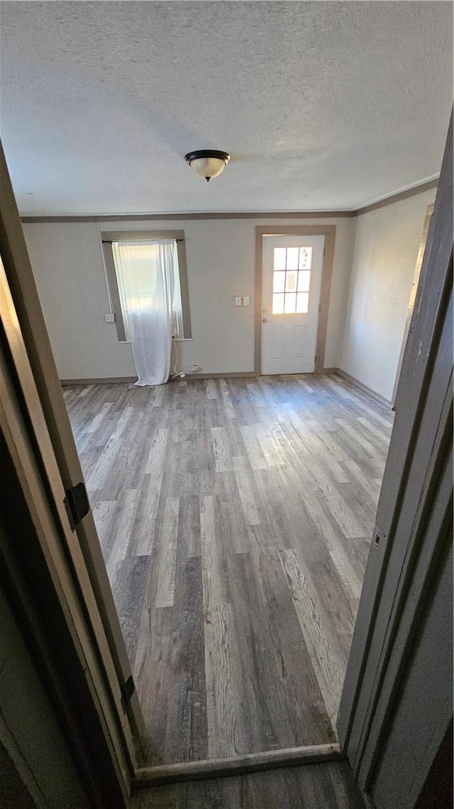 unfurnished room with a textured ceiling, wood finished floors, and crown molding