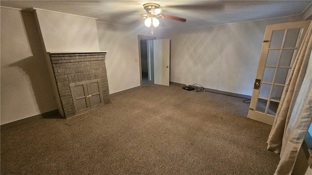 unfurnished living room with carpet floors, a brick fireplace, baseboards, and a ceiling fan