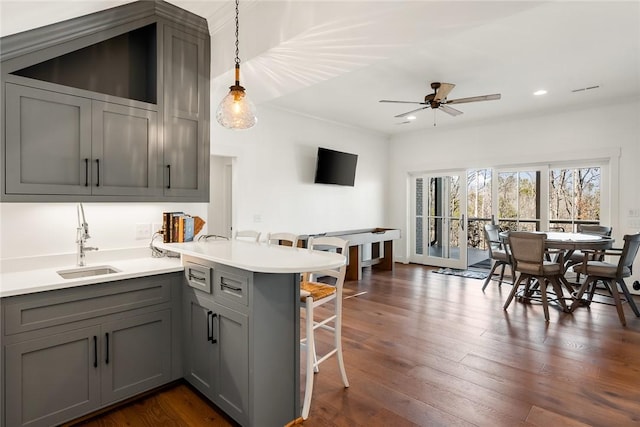 kitchen featuring dark wood-style flooring, gray cabinetry, a sink, a peninsula, and a kitchen breakfast bar