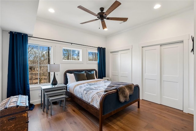 bedroom featuring wood finished floors, recessed lighting, two closets, and crown molding