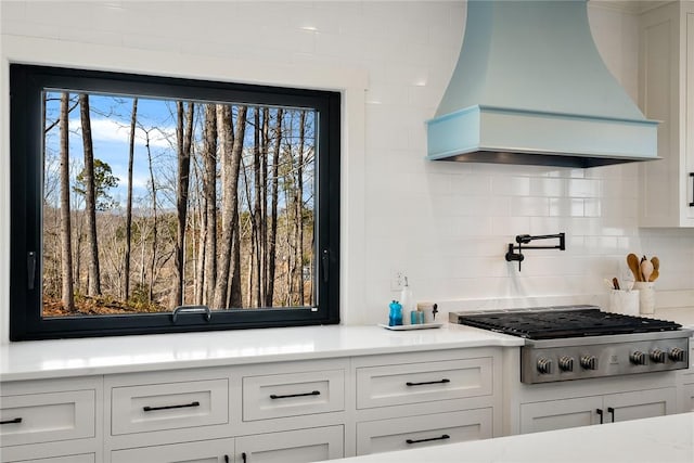 kitchen with stainless steel gas cooktop, custom exhaust hood, light countertops, backsplash, and white cabinetry