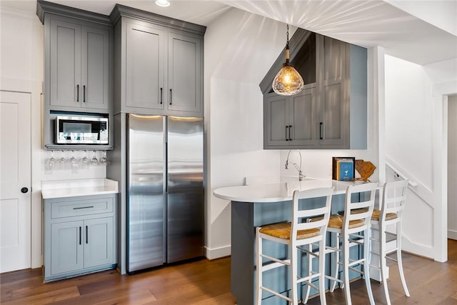 kitchen featuring stainless steel appliances, light countertops, gray cabinets, dark wood-style floors, and a kitchen bar